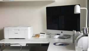 Bel tiskalnik na beli pisalni mizi skupaj z Applovim ekranom.